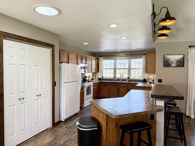 992 Trumble Creek Rd, Kalispell, MT 59901 - kitchen with white appliances, brown cabinets, dark wood-style flooring, a breakfast bar, and recessed lighting
