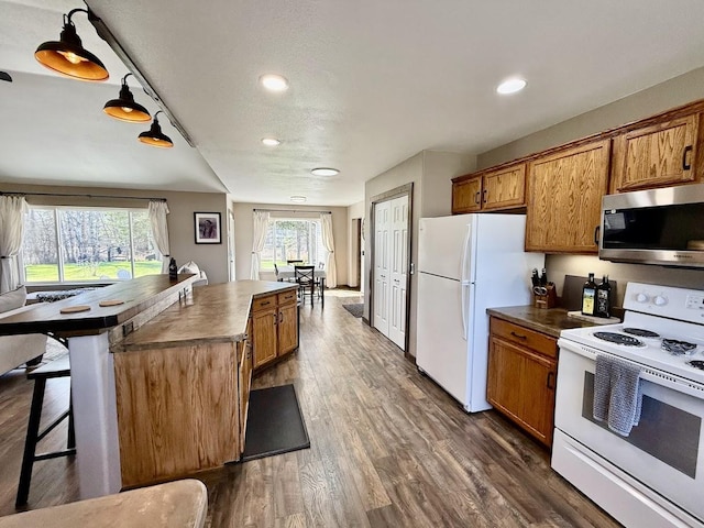 992 Trumble Creek Rd, Kalispell, MT 59901 - kitchen with white appliances, brown cabinetry, dark wood finished floors, recessed lighting, and a kitchen bar