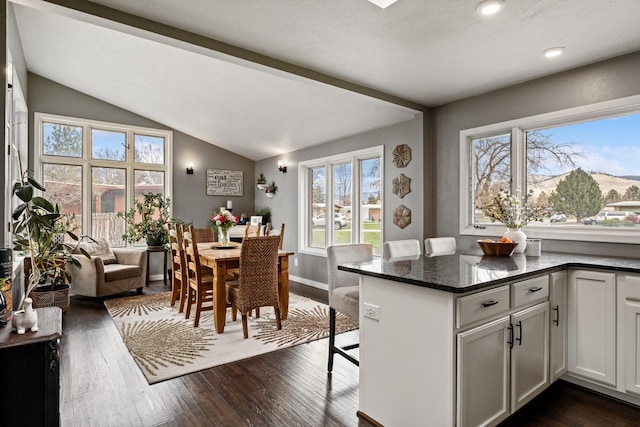 2324 Cloverdale Dr, Missoula, MT 59803 - kitchen featuring lofted ceiling, dark wood-style flooring, dark stone counters, a breakfast bar area, and white cabinetry