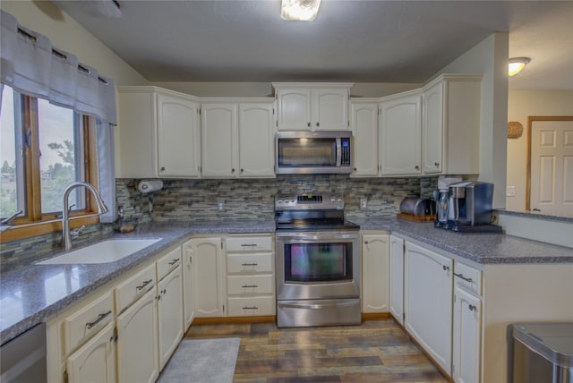 kitchen with a peninsula, dark wood-style floors, decorative backsplash, stainless steel appliances, and a sink
