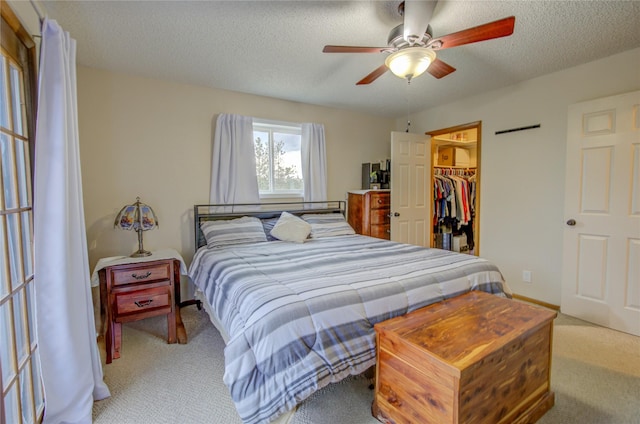 bedroom featuring a closet, carpet flooring, a textured ceiling, a walk in closet, and ceiling fan