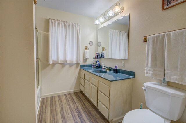 bathroom featuring vanity, baseboards, toilet, a shower, and wood finished floors