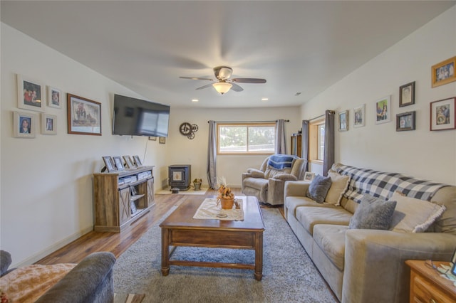 living area with a wood stove, a ceiling fan, recessed lighting, wood finished floors, and baseboards