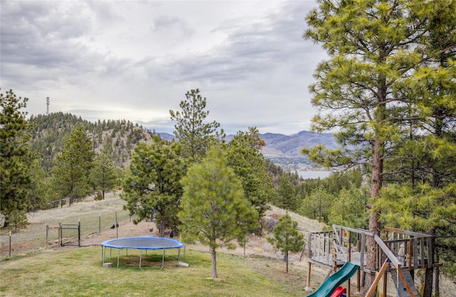 view of yard with a mountain view, fence, a trampoline, and a playground