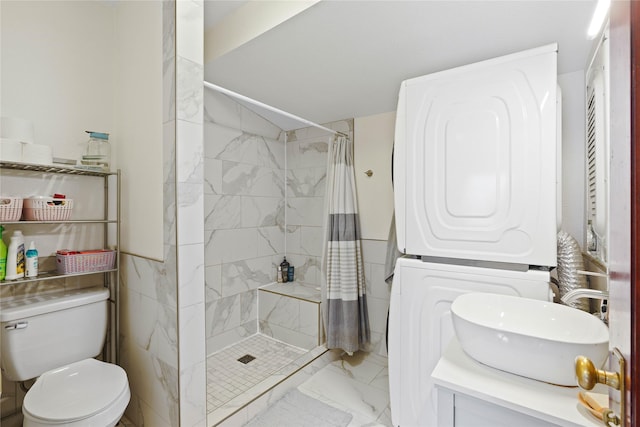 bathroom featuring marble finish floor, stacked washer and clothes dryer, a tile shower, and toilet