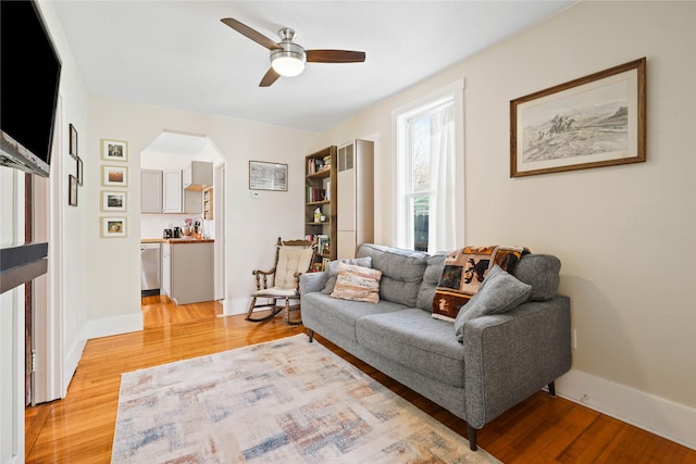 living room with baseboards, a ceiling fan, arched walkways, and light wood-style floors