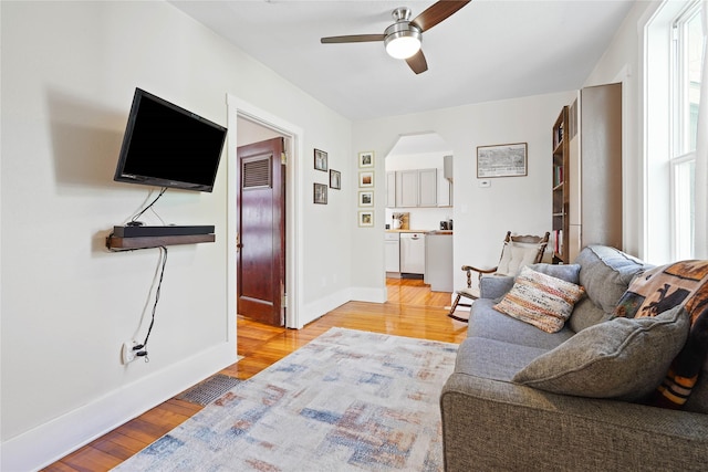 living room featuring light wood-style flooring, a ceiling fan, arched walkways, and baseboards
