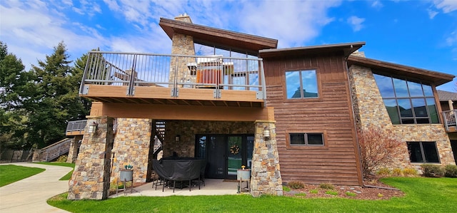 rear view of house featuring a balcony, a patio, and stone siding