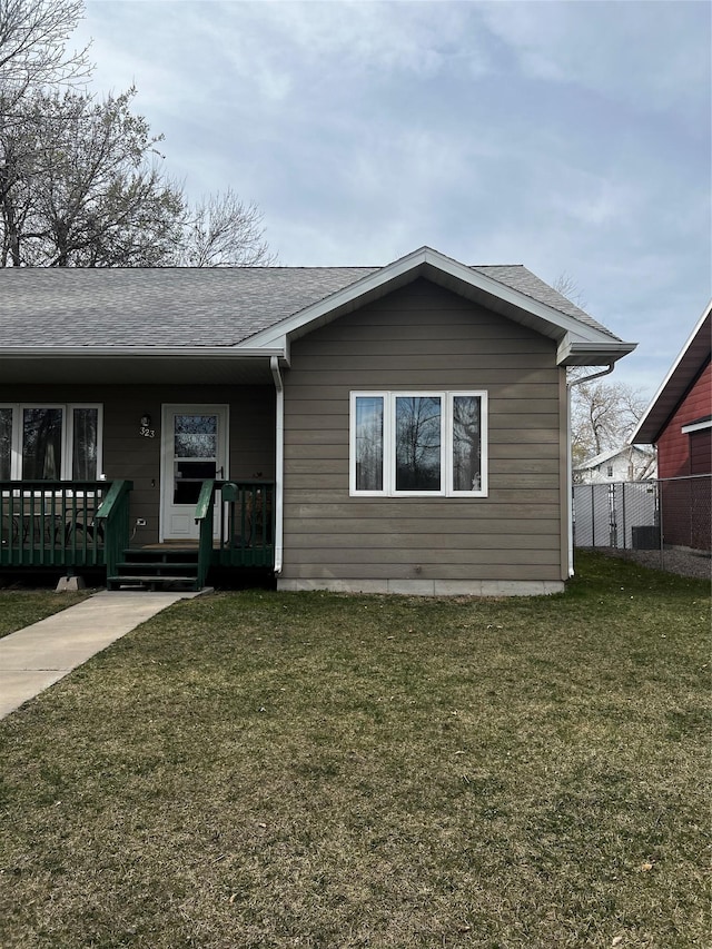 ranch-style house featuring roof with shingles, fence, and a front lawn