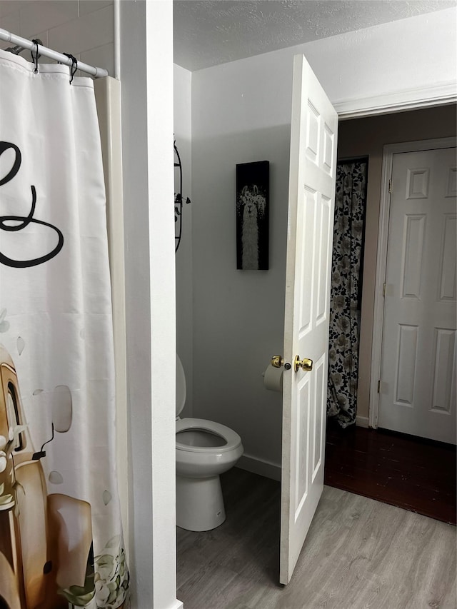 full bathroom featuring toilet, wood finished floors, baseboards, and a shower with shower curtain