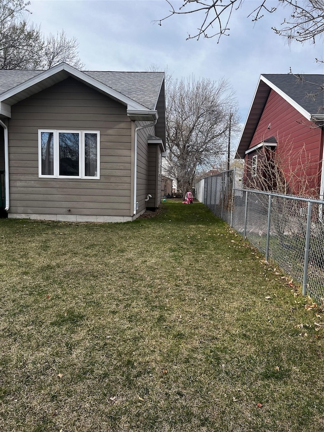 view of home's exterior featuring a yard, fence, and a shingled roof