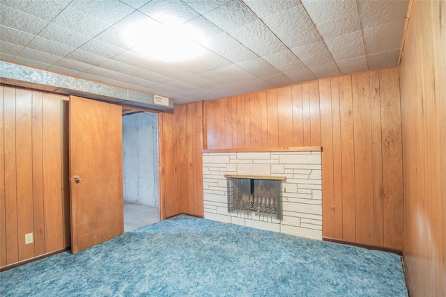 unfurnished living room featuring carpet, a stone fireplace, and wooden walls
