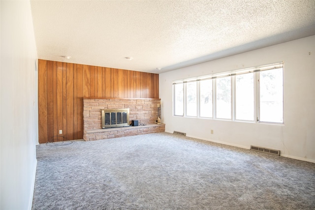 unfurnished living room featuring a textured ceiling, wood walls, carpet, and visible vents