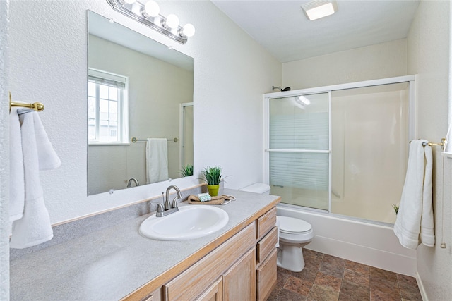 bathroom featuring stone finish floor, vanity, toilet, and enclosed tub / shower combo
