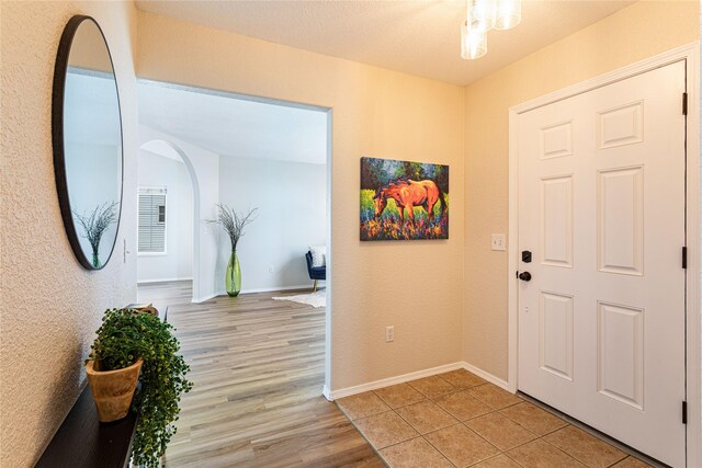 entryway with arched walkways, baseboards, and light wood-style floors