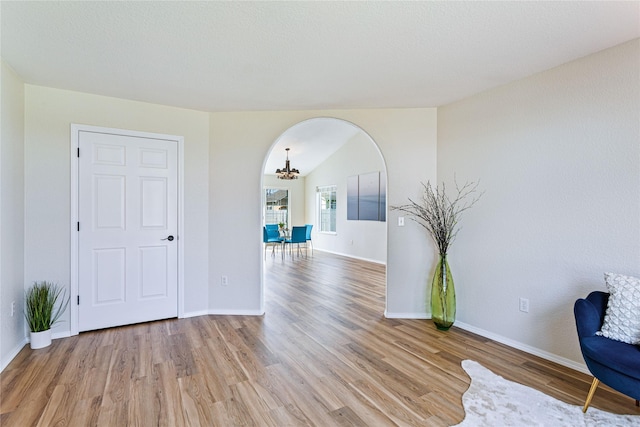 interior space featuring a chandelier, light wood-type flooring, baseboards, and arched walkways