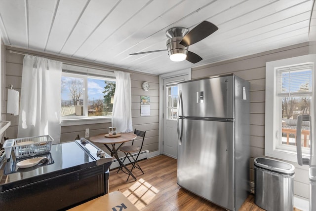 kitchen featuring a baseboard heating unit, freestanding refrigerator, wood finished floors, wood walls, and ceiling fan