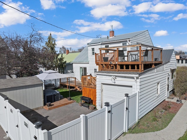 back of house with a deck, aphalt driveway, a gate, a fenced backyard, and metal roof