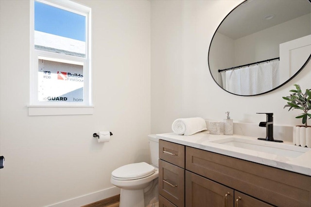 bathroom with baseboards, wood finished floors, vanity, and toilet