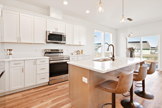 kitchen with a sink, light wood-type flooring, pendant lighting, stainless steel appliances, and white cabinets