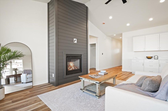 living area featuring light wood-type flooring, a ceiling fan, baseboards, and a large fireplace