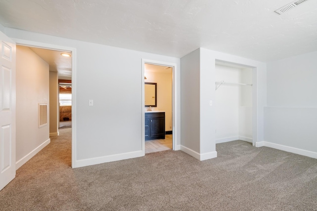 unfurnished bedroom with light colored carpet, baseboards, and ensuite bath