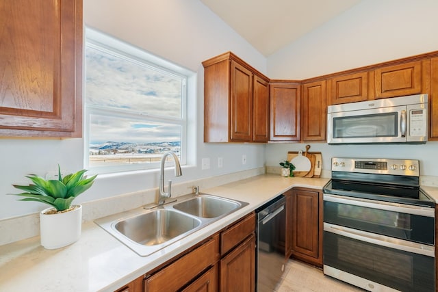 kitchen featuring stainless steel appliances, a sink, light countertops, vaulted ceiling, and brown cabinets