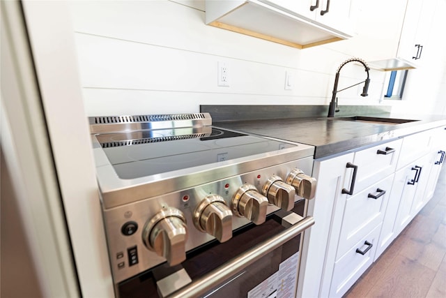 room details featuring dark countertops, wood finished floors, a sink, stainless steel range, and white cabinets