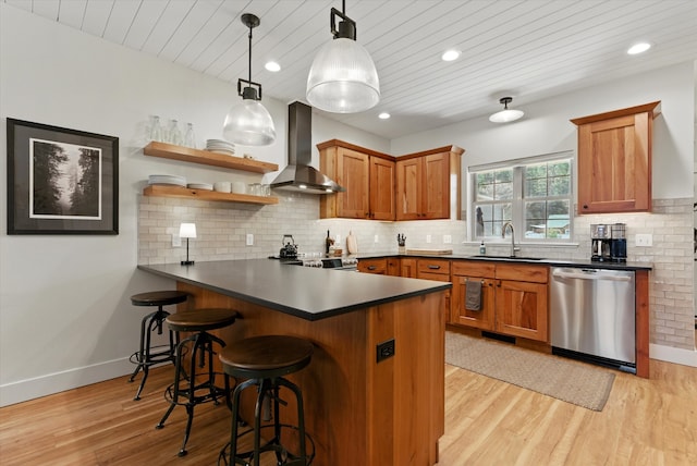 kitchen with stainless steel dishwasher, a sink, wall chimney exhaust hood, a peninsula, and brown cabinetry