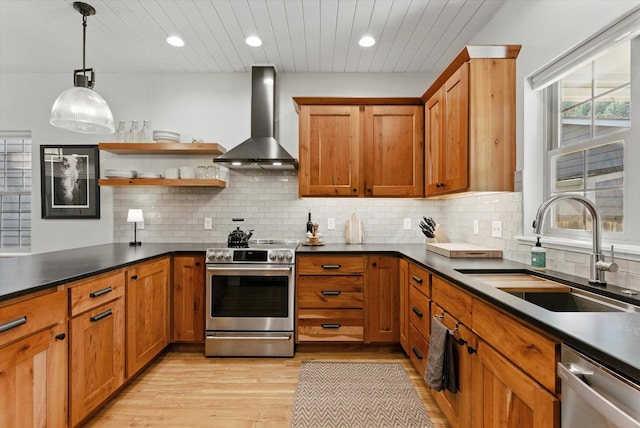 kitchen featuring wall chimney range hood, dark countertops, a sink, light wood-style floors, and stainless steel appliances
