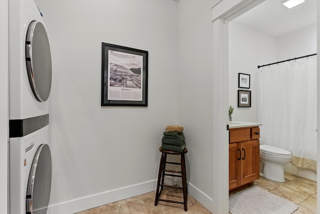 bathroom featuring tile patterned floors, toilet, vanity, stacked washing maching and dryer, and baseboards
