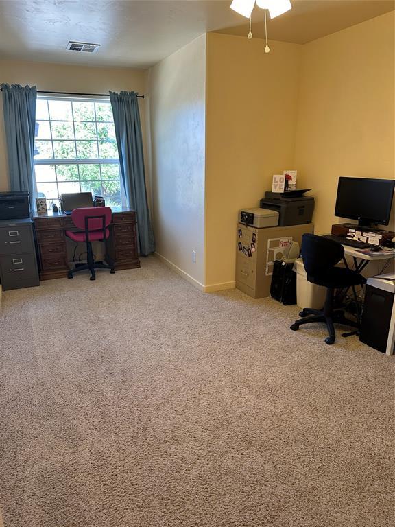 carpeted office space featuring visible vents, ceiling fan, and baseboards