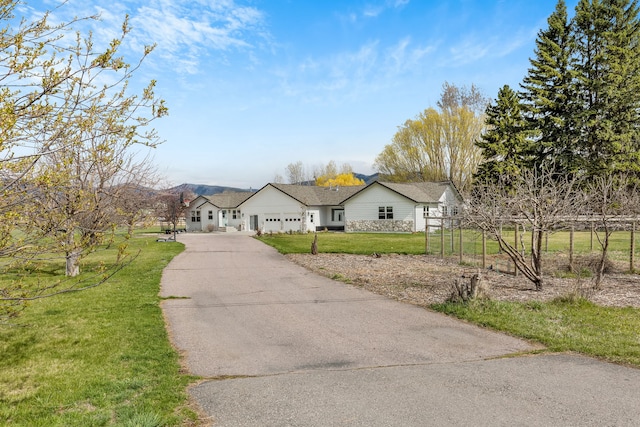 ranch-style house with stone siding, a front lawn, aphalt driveway, and a garage