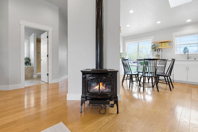 dining space featuring recessed lighting, a wood stove, light wood-type flooring, a skylight, and baseboards