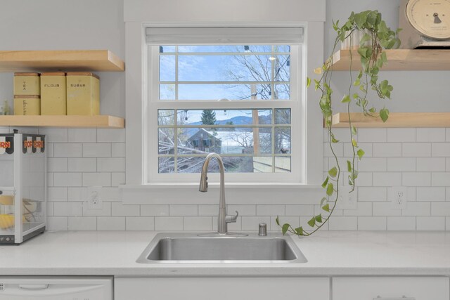 kitchen with open shelves, backsplash, dishwasher, and a sink