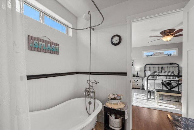 full bath featuring a ceiling fan, a freestanding tub, a wainscoted wall, and wood finished floors
