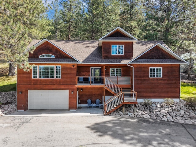 rustic home with an attached garage, driveway, roof with shingles, and stairway