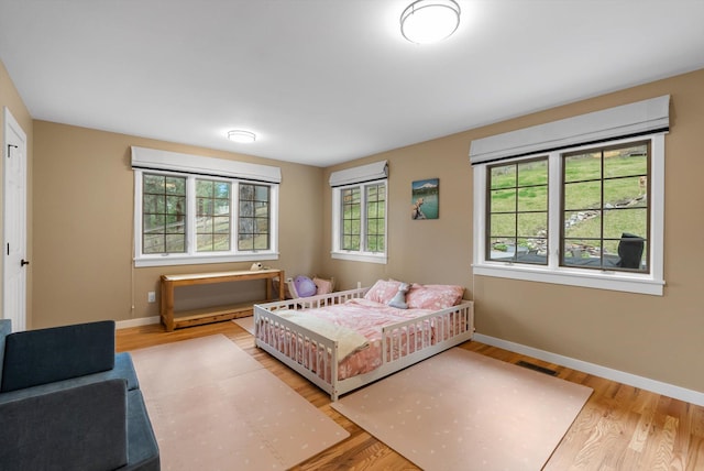 bedroom featuring baseboards, visible vents, wood finished floors, and a wall mounted AC