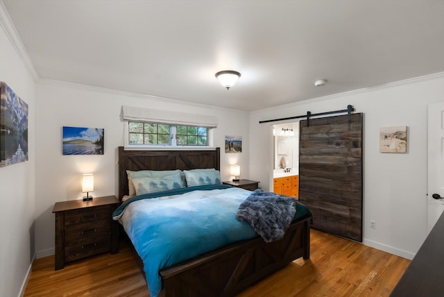 bedroom featuring a barn door, wood finished floors, crown molding, baseboards, and ensuite bathroom