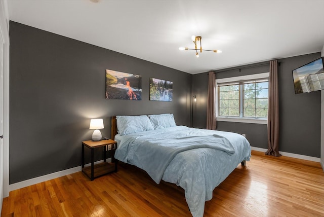 bedroom with baseboards, a chandelier, and light wood-style flooring