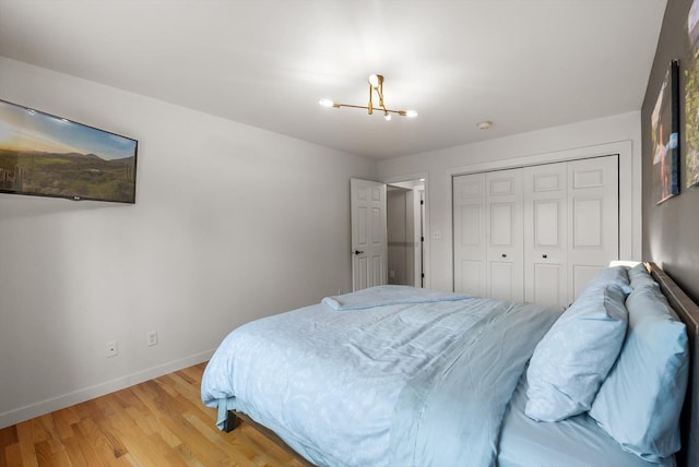 bedroom with a closet, baseboards, light wood-style flooring, and an inviting chandelier