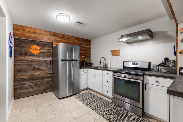 kitchen featuring wall chimney exhaust hood, a sink, dark countertops, visible vents, and appliances with stainless steel finishes