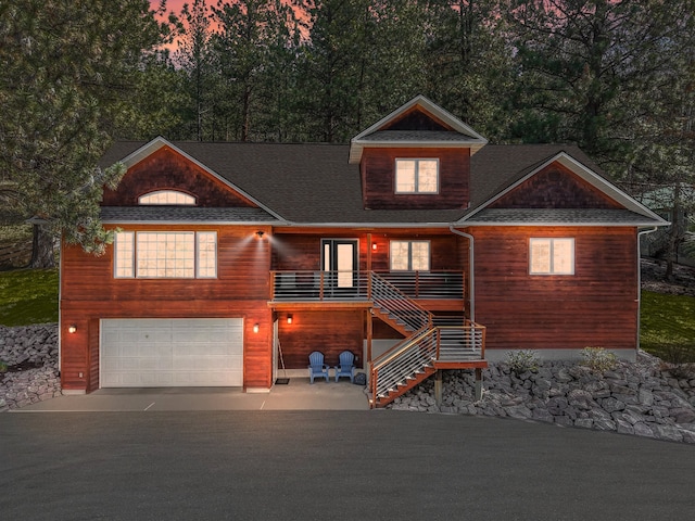 rustic home featuring an attached garage, a shingled roof, concrete driveway, and stairway