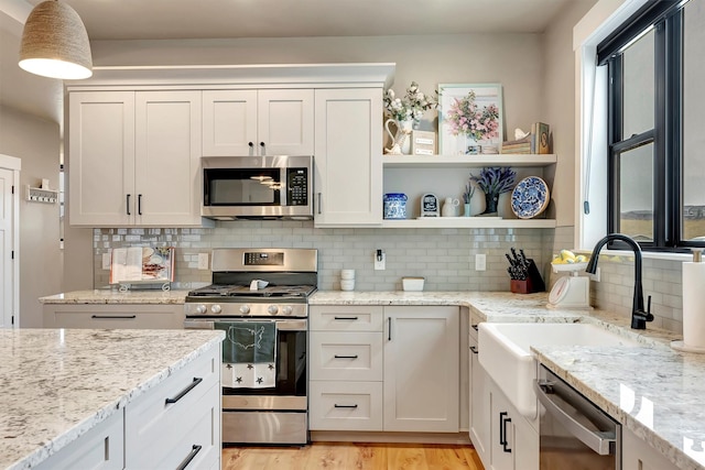 kitchen featuring light wood finished floors, a sink, backsplash, light stone countertops, and appliances with stainless steel finishes