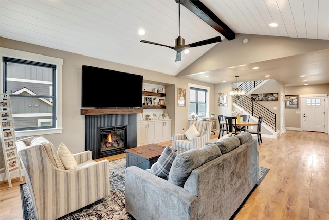 living area with a glass covered fireplace, light wood-type flooring, a wealth of natural light, and vaulted ceiling with beams