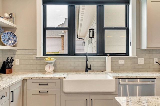 kitchen featuring light stone countertops, dishwasher, a sink, and tasteful backsplash