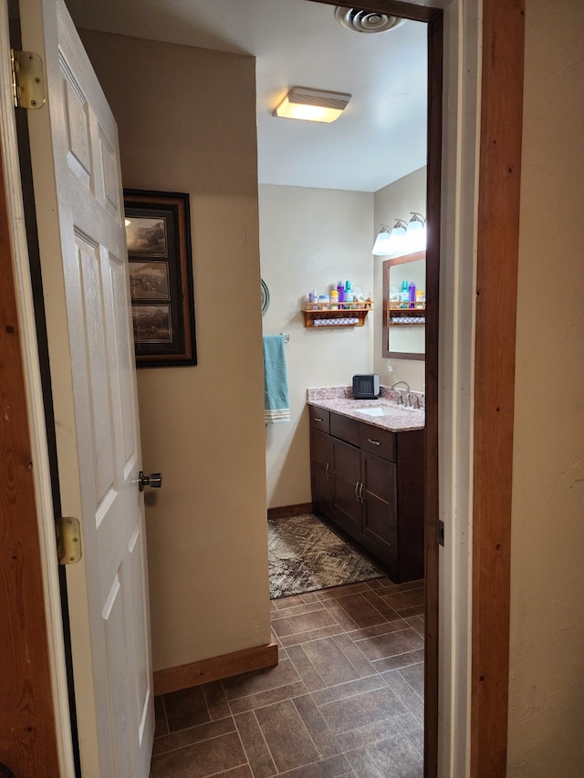 bathroom featuring baseboards, stone finish floor, and vanity
