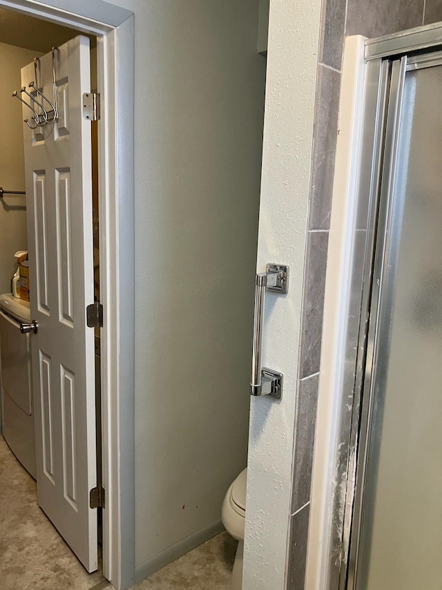 bathroom featuring a shower with door, washer / dryer, and toilet