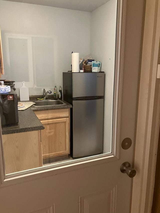 kitchen featuring freestanding refrigerator, a sink, light brown cabinetry, and dark countertops