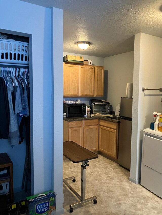 kitchen with washer / clothes dryer, black microwave, dark countertops, a toaster, and freestanding refrigerator